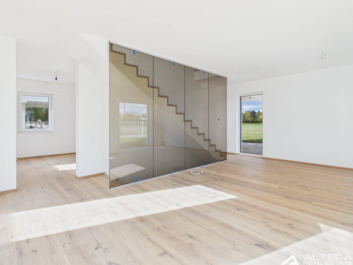 Helles Wohnzimmer mit Holzboden und einer eleganten Glaswand, die den Treppenbereich abtrennt.
