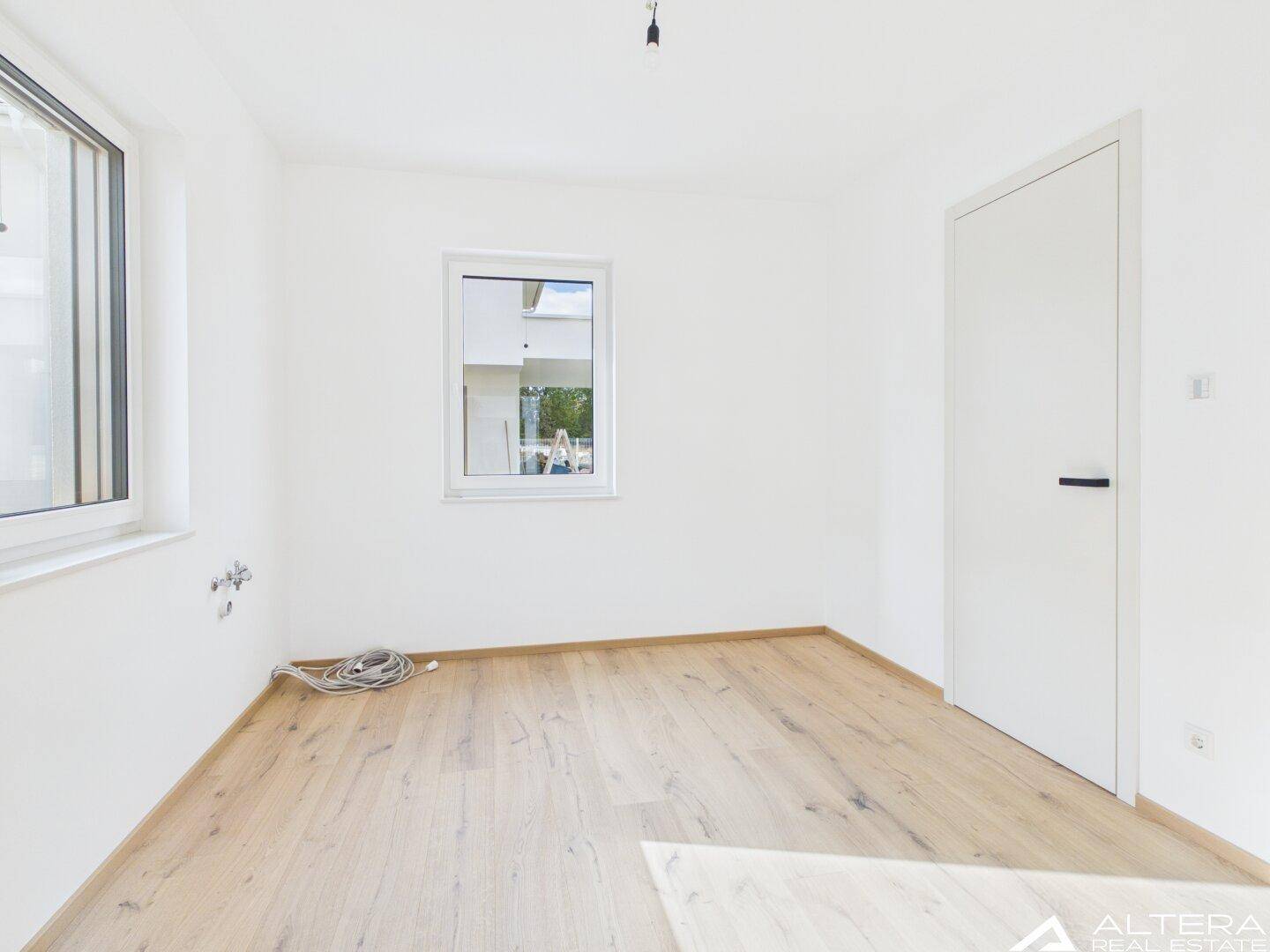 Helles Zimmer mit Holzboden und zwei Fenstern, bereit zur individuellen Gestaltung.