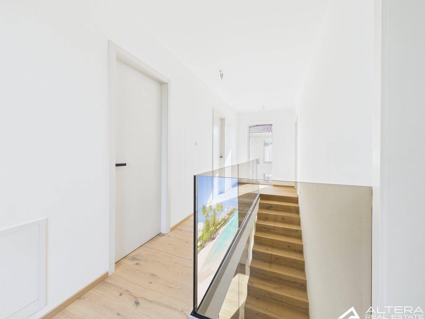 Obergeschoss-Flur mit Holzboden und modernem Glasgeländer, das die Treppe säumt.