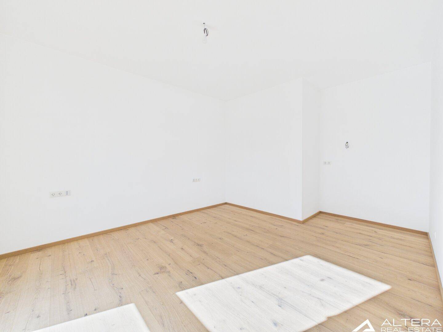 Leeres Zimmer mit Holzboden und weiß gestrichenen Wänden, ideal für ein Schlafzimmer.