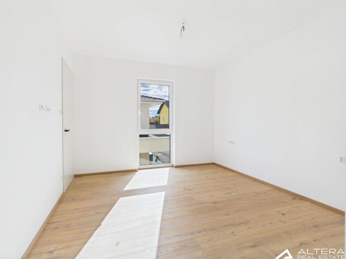 Helles Schlafzimmer mit Holzboden und großem Fenster, das viel Licht hereinlässt.