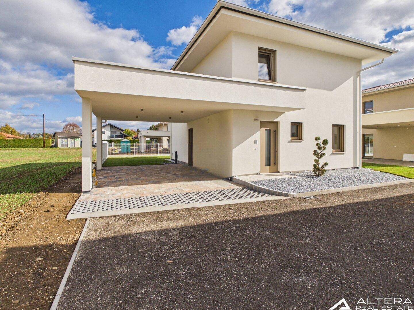 Seitenansicht des Hauses mit Carport und Zufahrt, umgeben von Grünflächen.