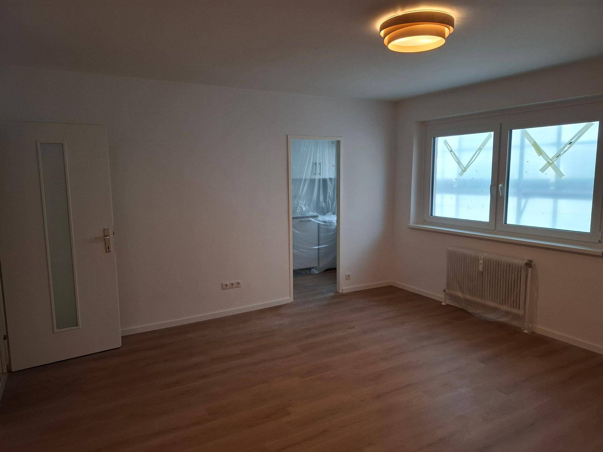 Heller, leerer Raum mit Laminatboden und großem Fenster, bereit zur individuellen Gestaltung.