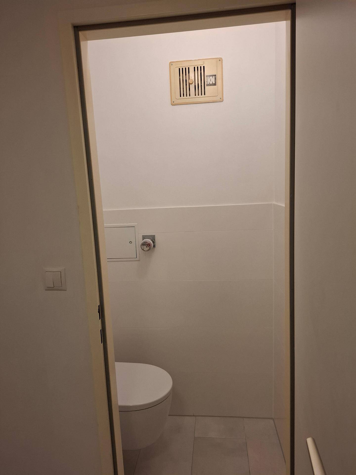 Modernes Gäste-WC mit wandhängender Toilette, Fliesenboden und Abluftventilator.
