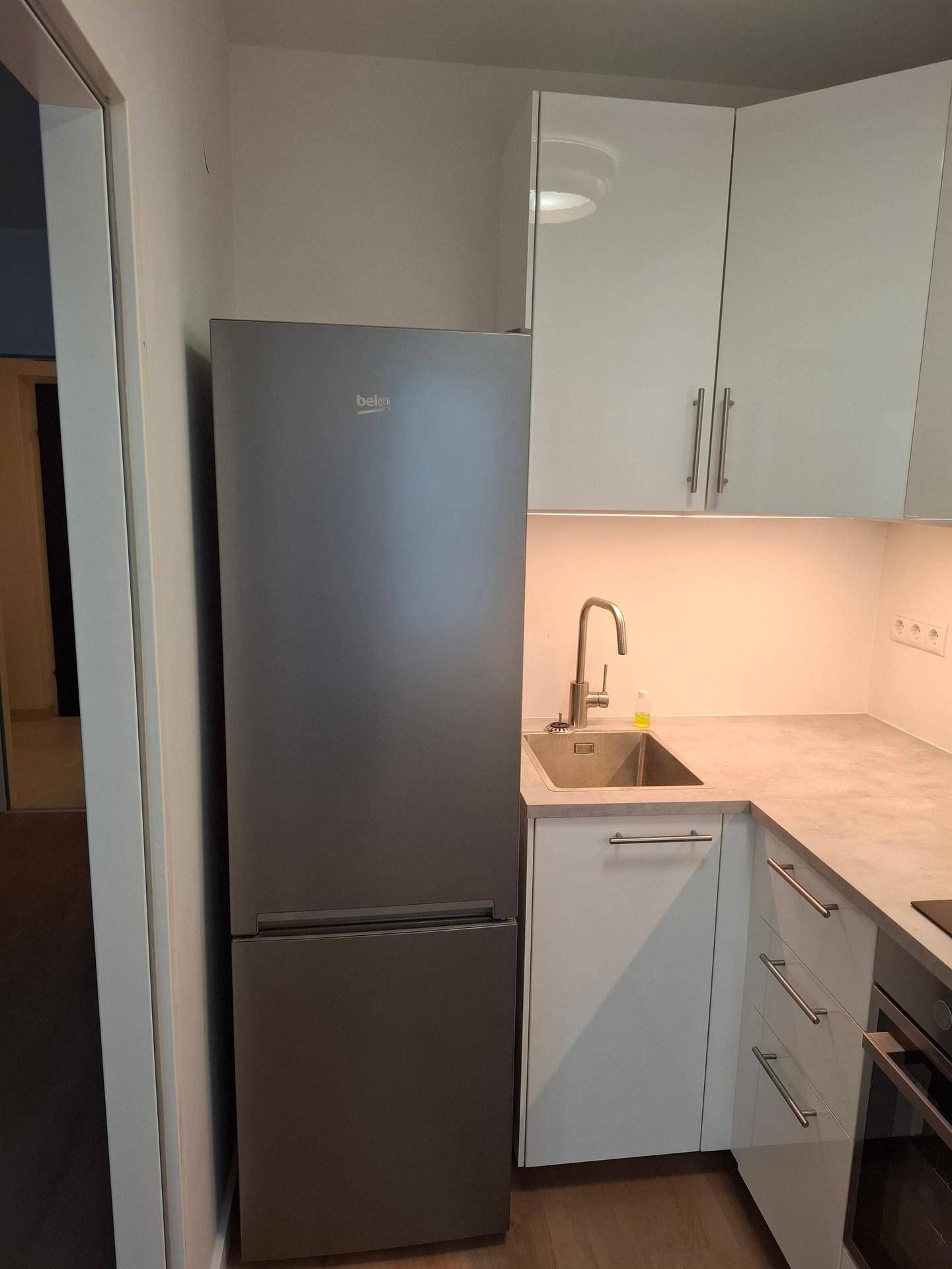 Funktionale Küche mit großem Kühlschrank, Spüle und weißen Oberschränken, gut ausgestattet.