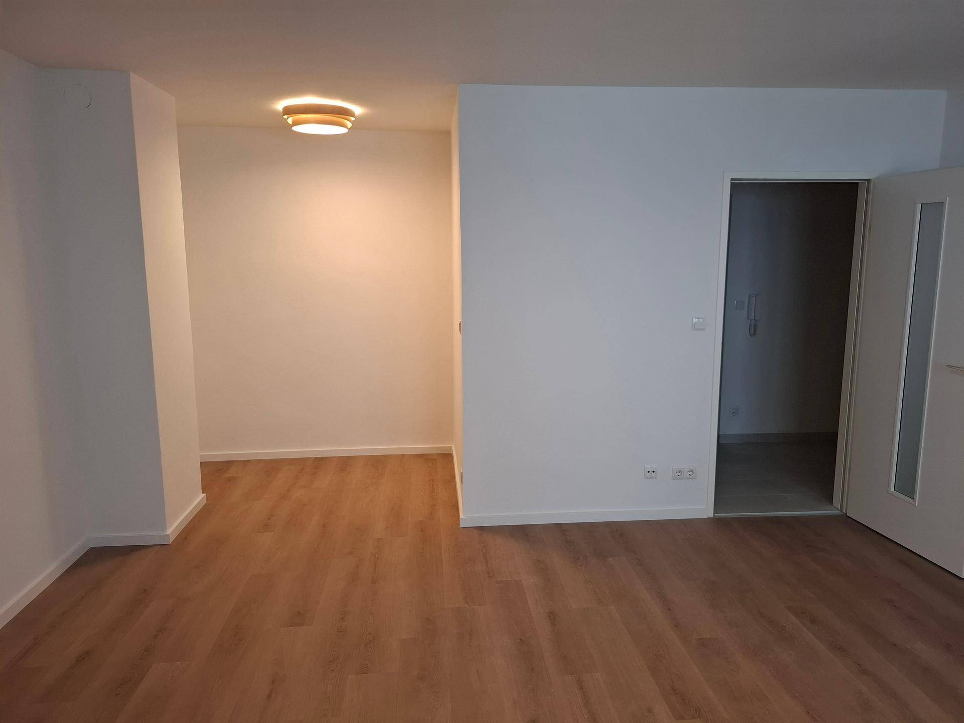 Leerer Wohnbereich mit hellem Laminatboden und weiß gestrichenen Wänden, bereit zum Einzug.