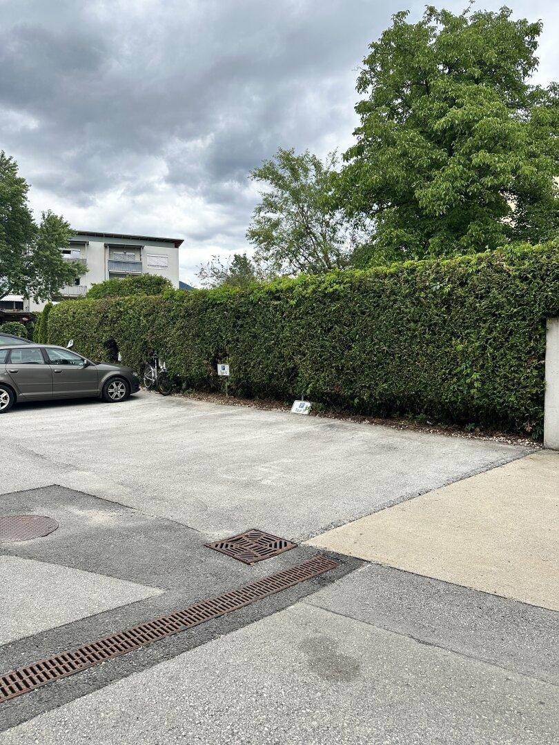 Außenparkplätze mit einem geparkten Auto und einer dichten Hecke vor einem Gebäude.