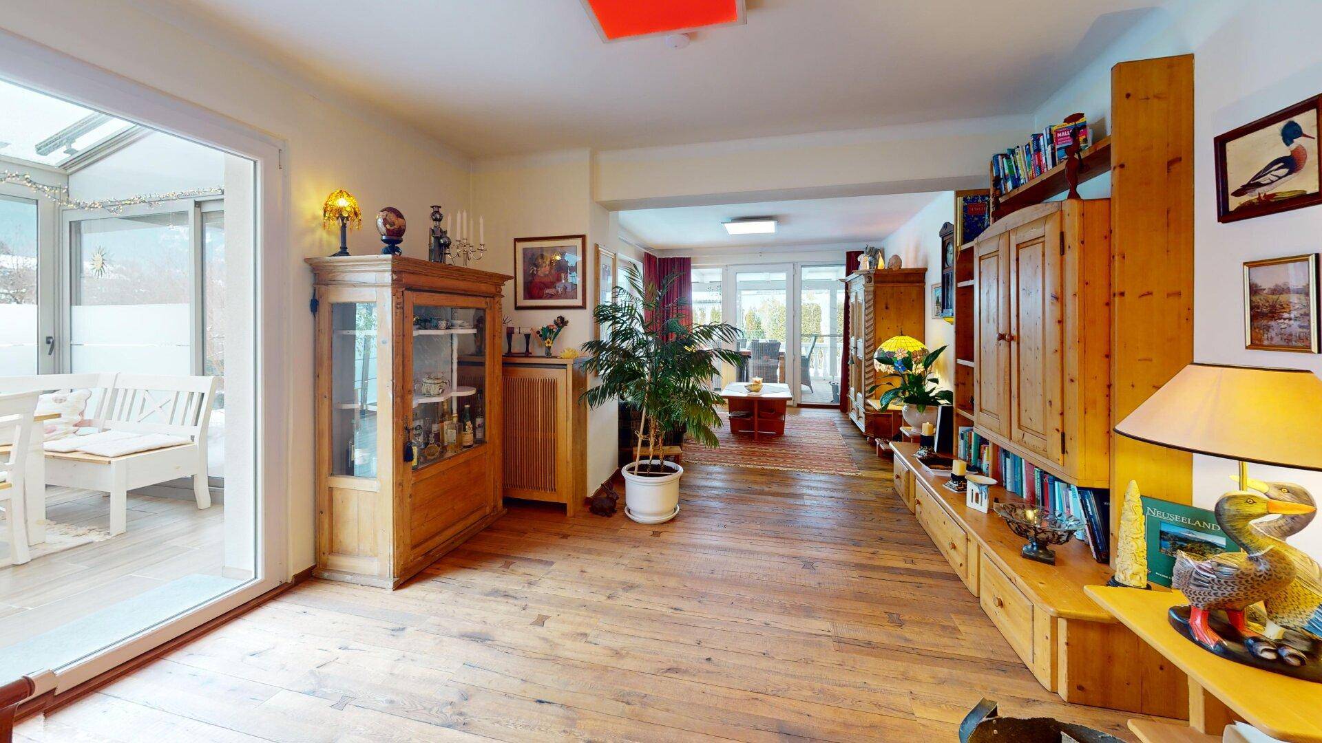 Geräumiges Wohnzimmer mit Holzdielenboden, Bücherregalen und direktem Zugang zum Wintergarten.