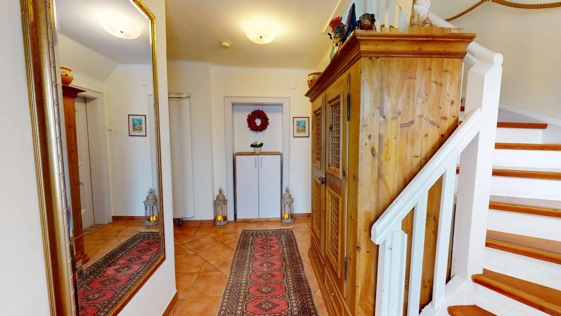 Heller Eingangsbereich mit Terrakottafliesen, großem Spiegel und Holztreppe zum Obergeschoss.