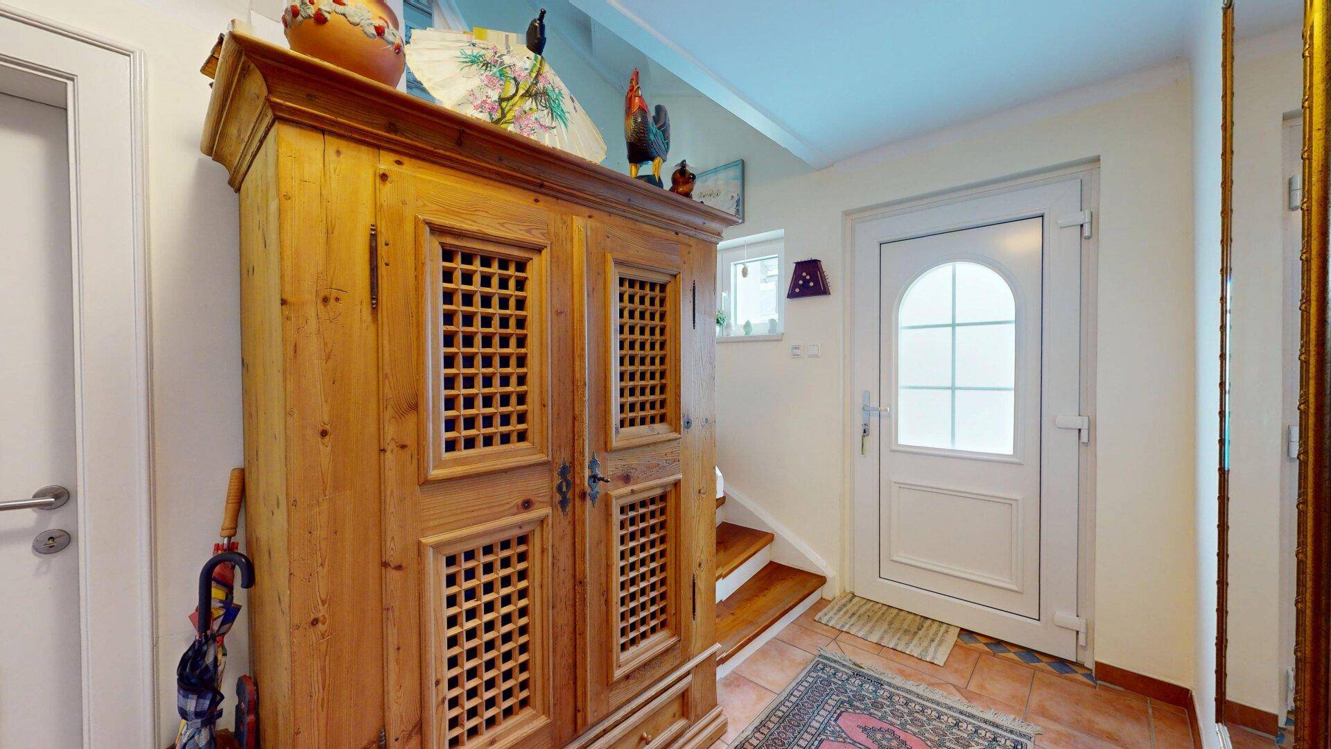 Eingangsbereich mit traditionellem Holzschrank, heller Eingangstür und Treppe zum Obergeschoss.