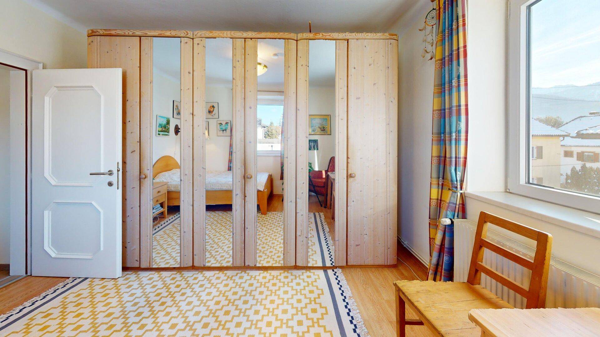 Helles Schlafzimmer im Dachgeschoss mit Spiegelschränken und Blick auf die Umgebung.