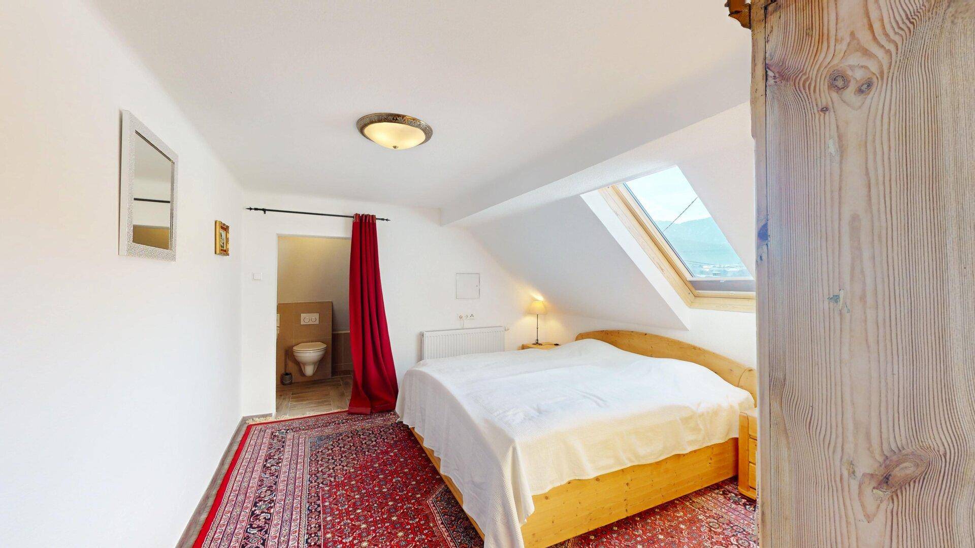 Gemütliches Schlafzimmer im Dachgeschoss mit Dachfenster und angrenzendem WC.
