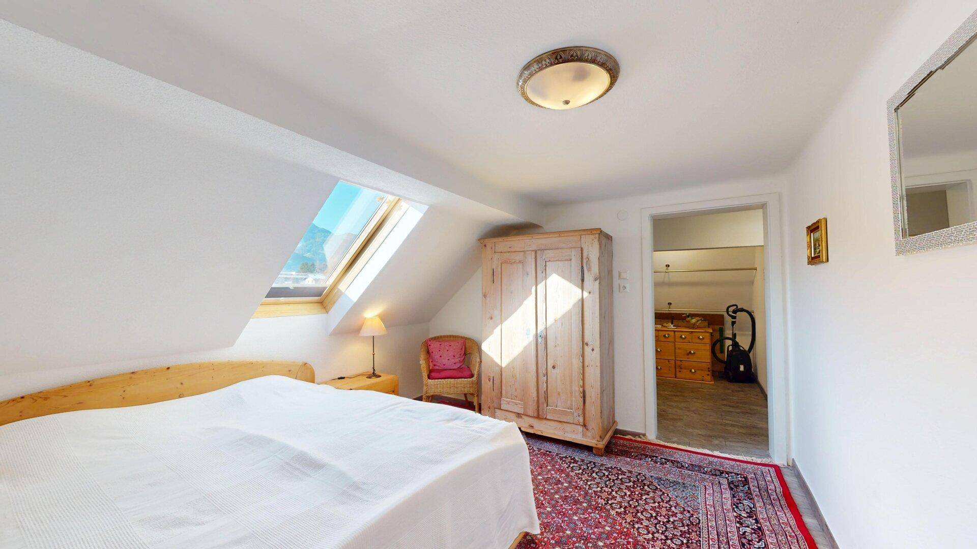 Schlafzimmer im Dachgeschoss mit Dachfenster, Holzschrank und Blick auf die Berge.