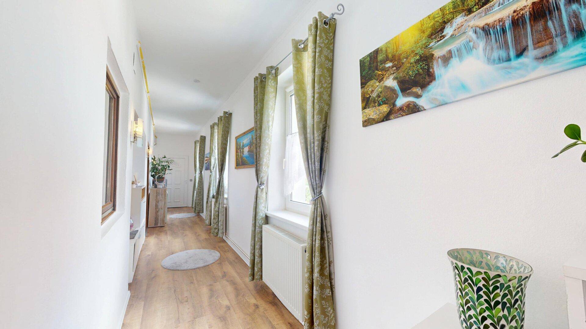 Heller Flur mit Holzboden, grünen Vorhängen und einem Wasserfallbild an der Wand.