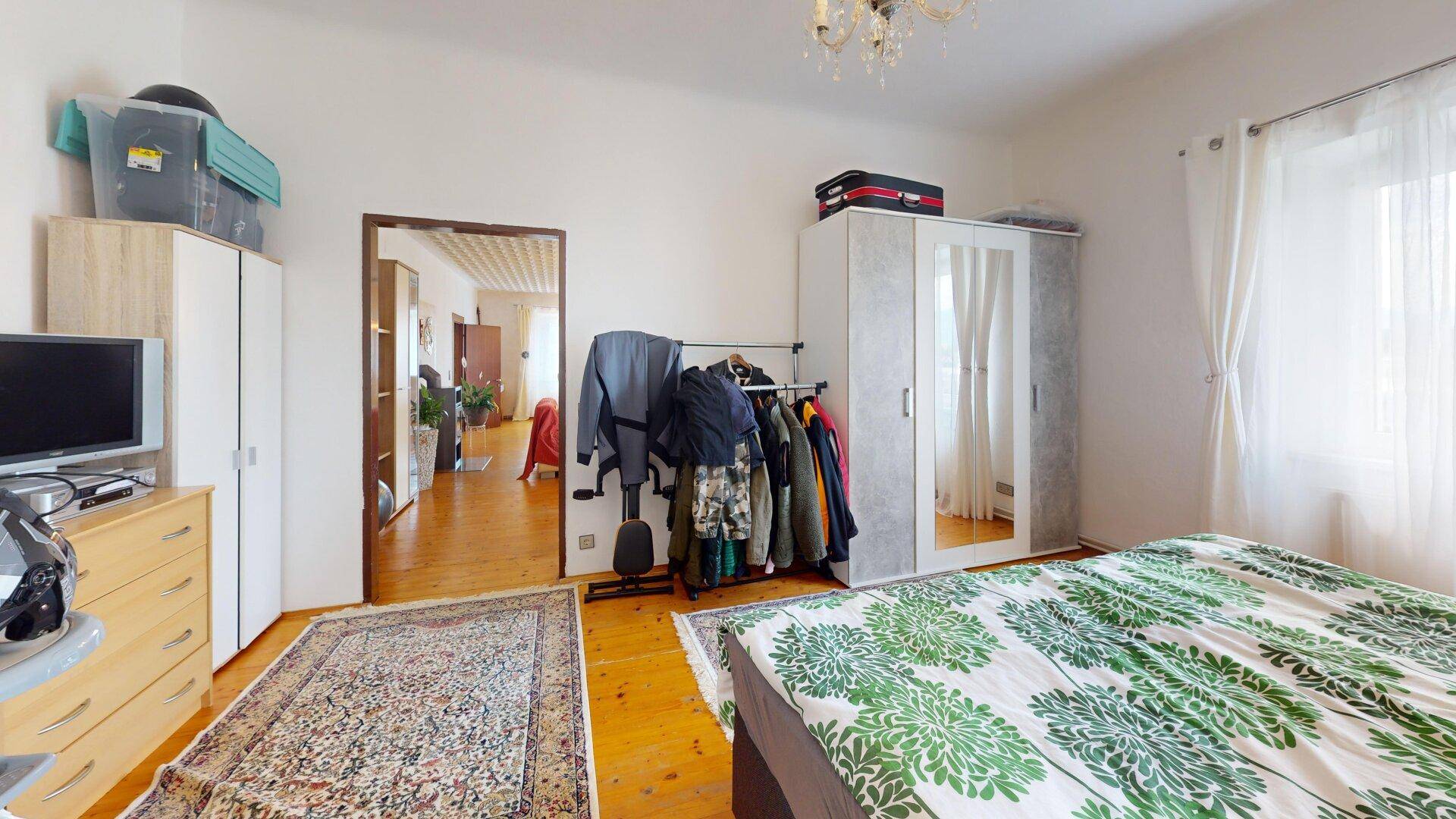 Schlafzimmer mit Holzboden, Kleiderschrank und Zugang zu einem weiteren Raum, hell und funktional.