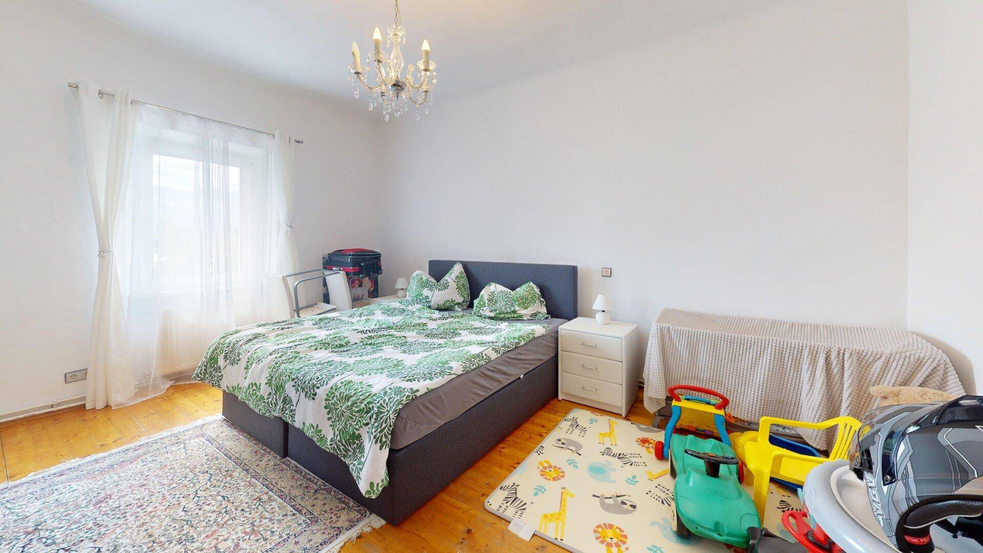 Helles Schlafzimmer mit Doppelbett, Holzboden und Spielbereich für Kinder, gemütlich eingerichtet.