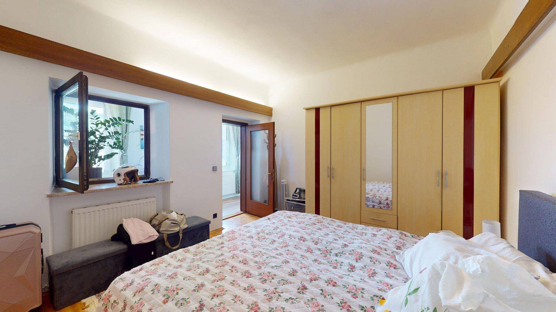 Gemütliches Schlafzimmer mit Holzbalken, großem Bett und Kleiderschrank, mit Fensterblick.