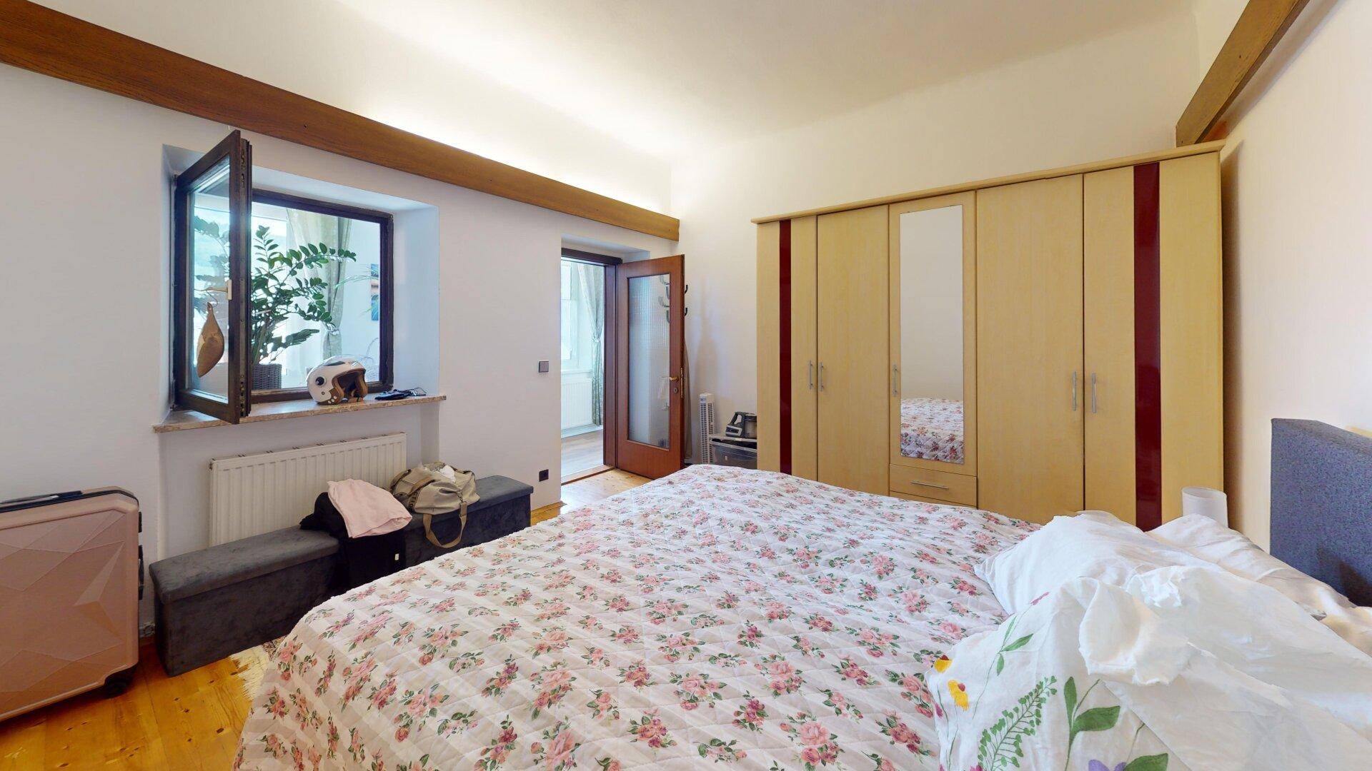 Helles Schlafzimmer mit Holzbalken, großem Bett und Kleiderschrank, mit Fensterblick.