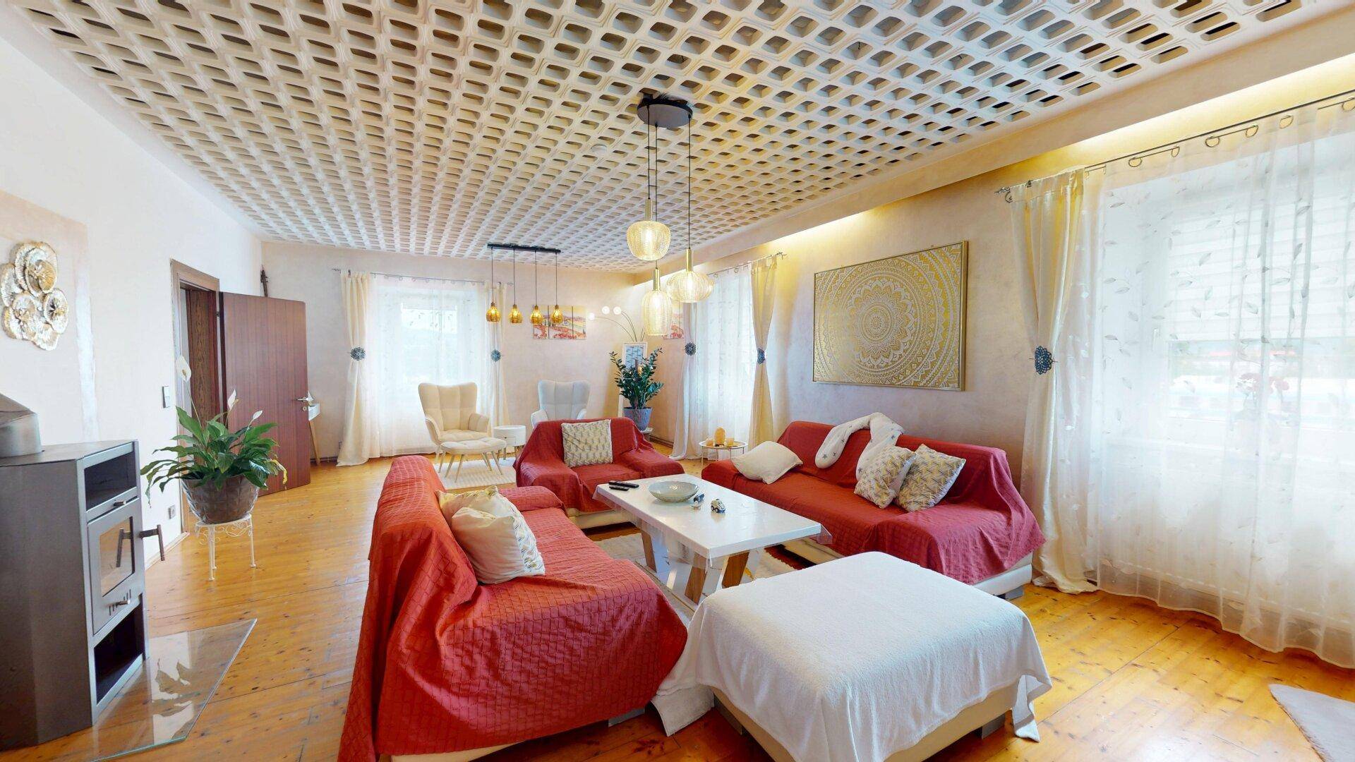 Geräumiges Wohnzimmer mit Holzboden, Kaminofen und dekorativer Deckenverkleidung, hell und einladend.
