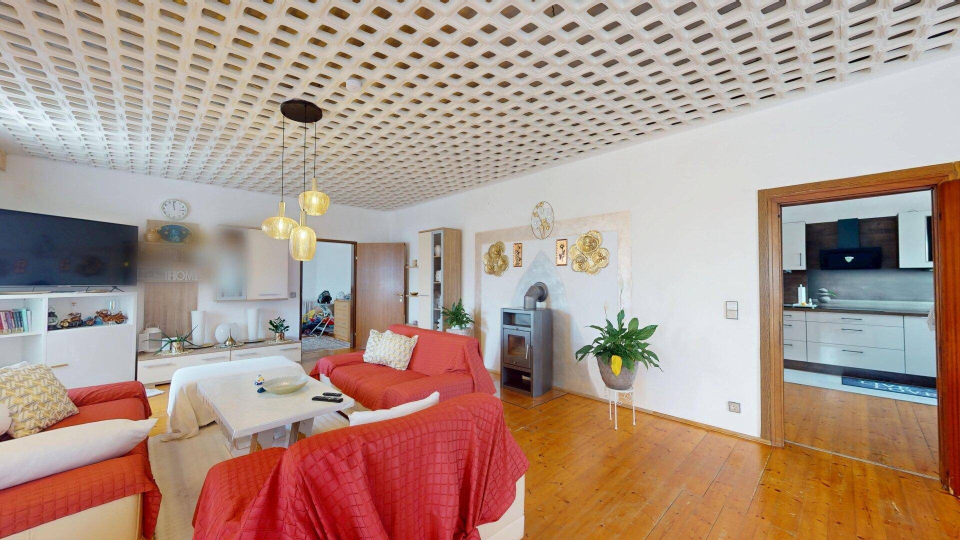 Helles Wohnzimmer mit Holzboden, Kaminofen und dekorativer Deckenverkleidung, einladend gestaltet.