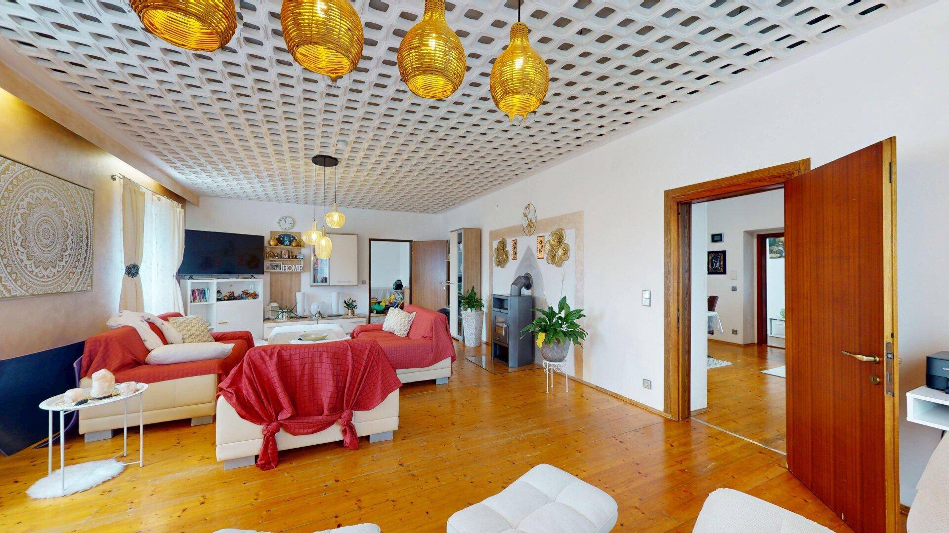 Geräumiges Wohnzimmer mit Holzboden, Kaminofen und dekorativer Deckenverkleidung, hell und einladend.