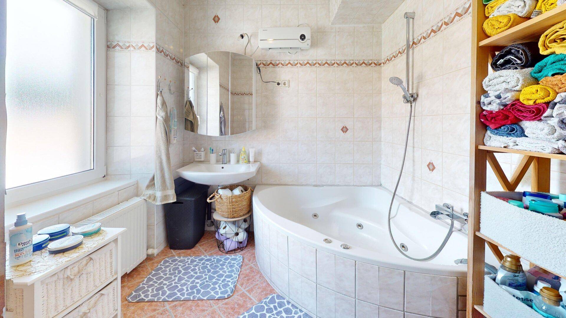 Helles Badezimmer mit Eckbadewanne, Dusche und Fenster, ausgestattet mit hellen Fliesen.