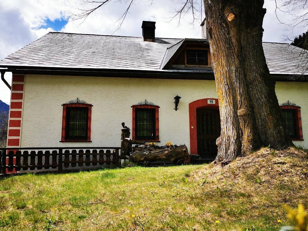 Traditionelles Haus mit weißer Fassade, roten Fensterrahmen und einem alten Baum im Vordergrund.