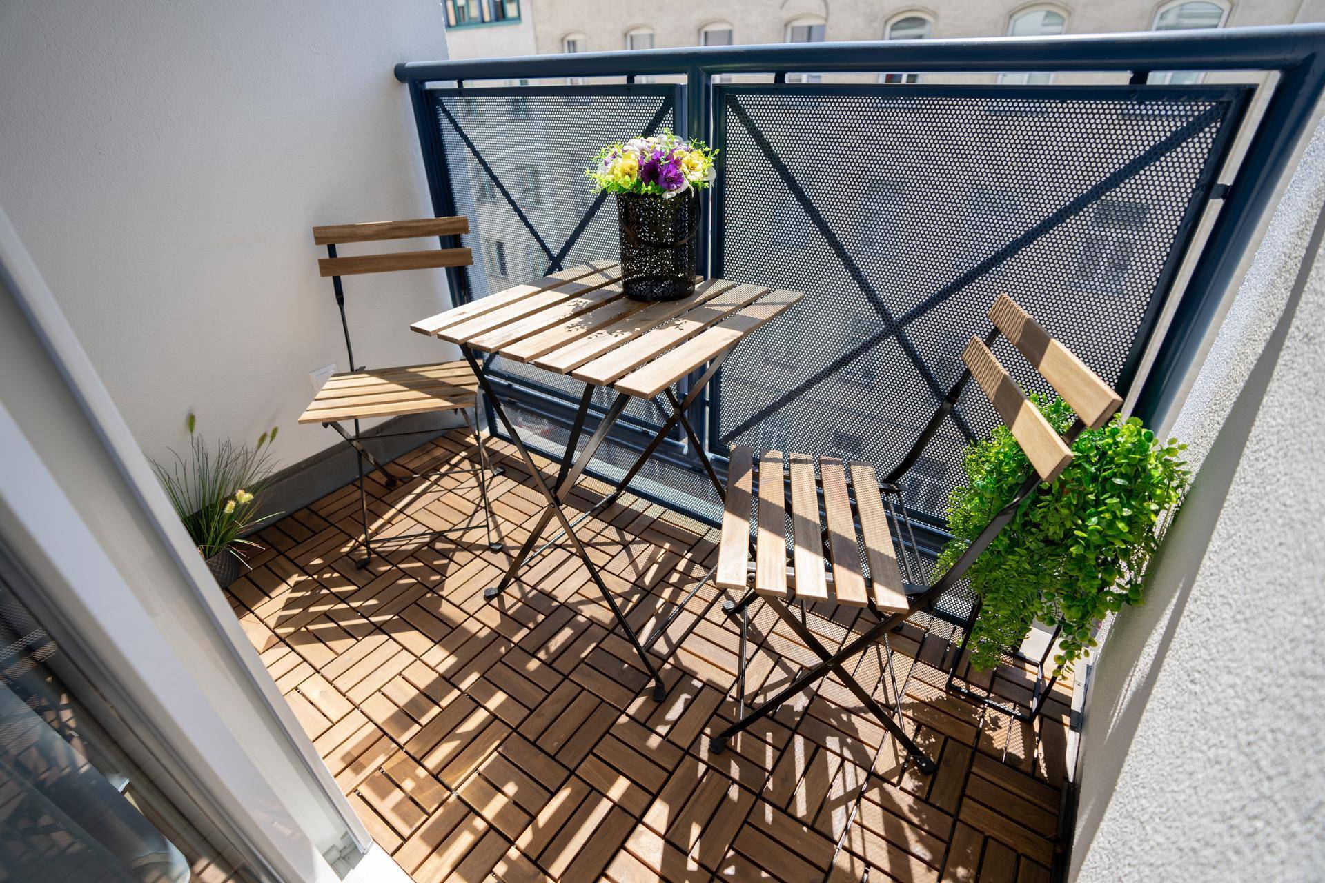 Sonniger Balkon mit Holzbodenfliesen, Sitzgelegenheiten und Blick auf die Stadt.