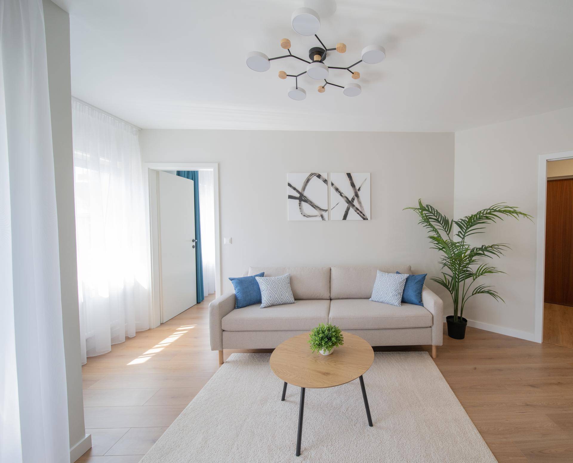 Helles Wohnzimmer mit beigem Sofa, Holzboden und moderner Deckenleuchte.