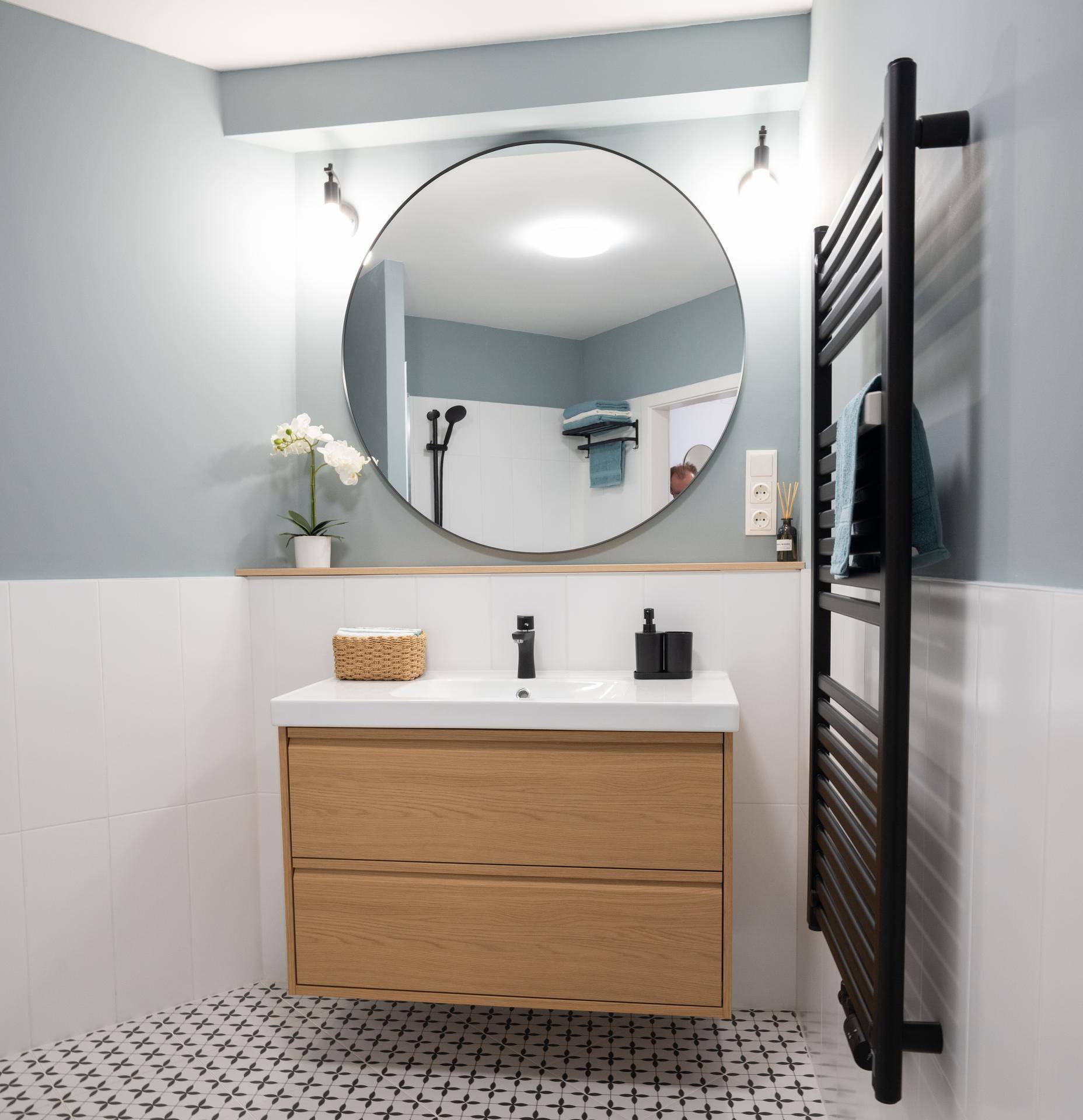 Modernes Badezimmer mit schwebendem Waschtisch, rundem Spiegel und Handtuchheizkörper.