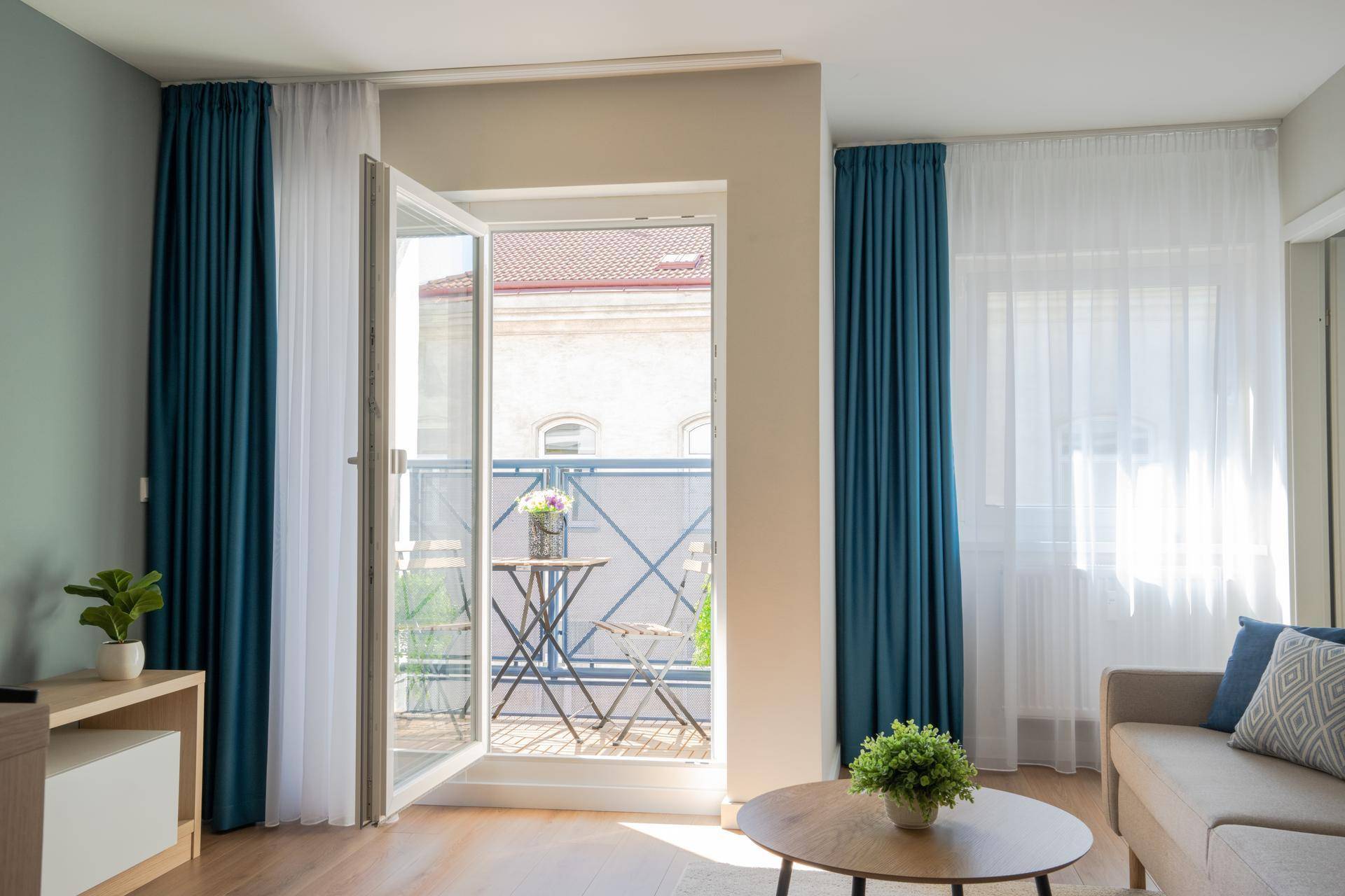 Blick vom Wohnzimmer auf den möblierten Balkon mit Holzboden und Stadtansicht.