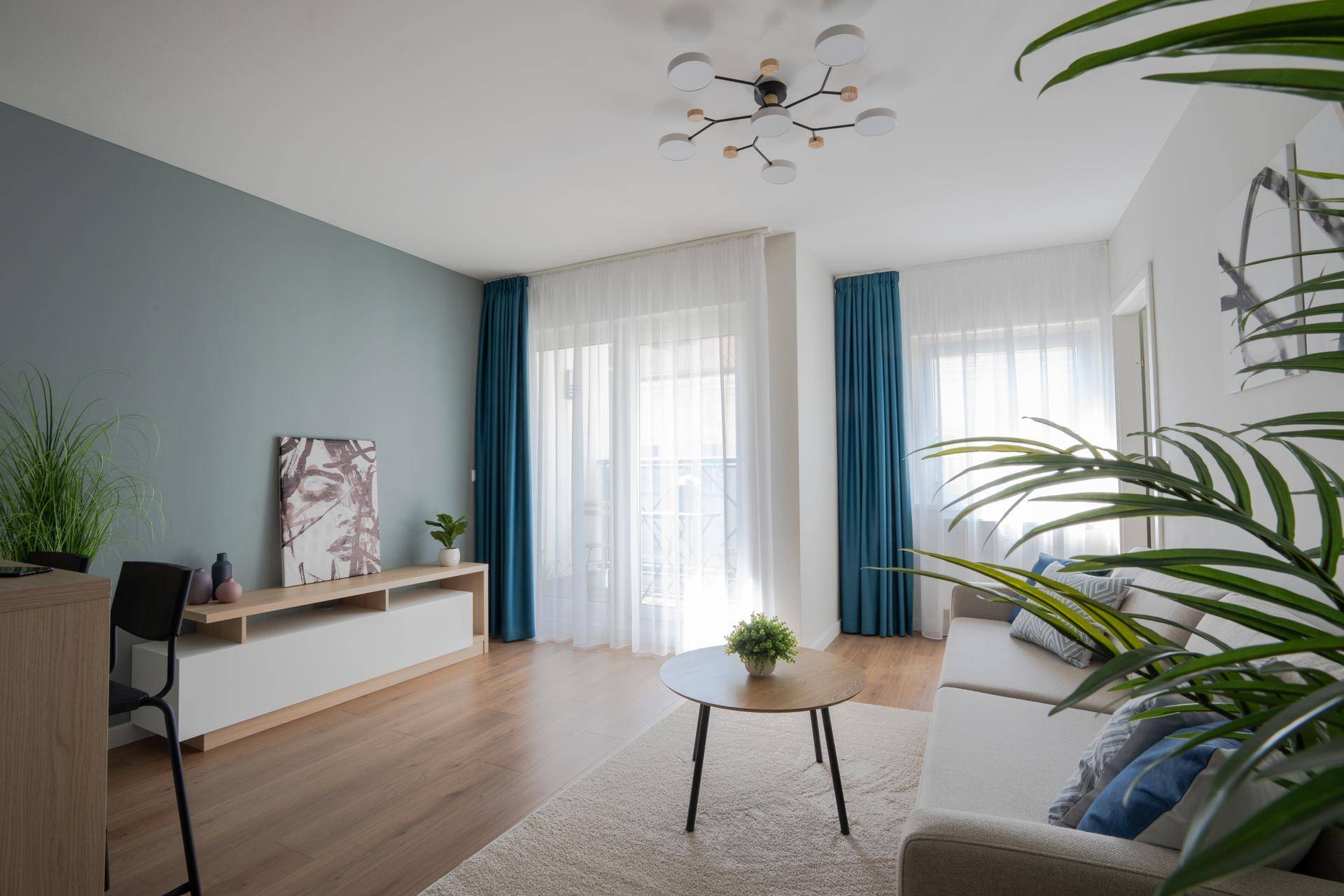 Geräumiges Wohnzimmer mit Holzboden, blauen Vorhängen und Zugang zum Balkon.