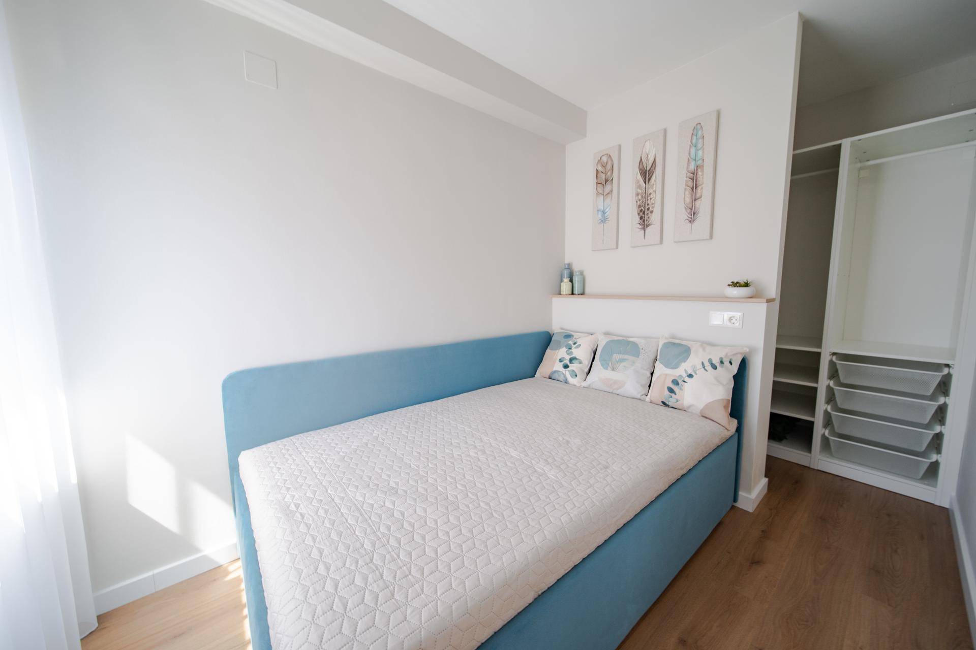 Schlafzimmer mit Einzelbett, Holzboden und offenem Kleiderschrank.