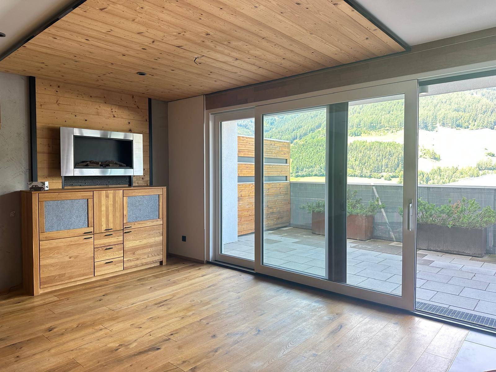 Helles Wohnzimmer mit Holzboden, Holzdecke und großen Schiebetüren zur Terrasse mit Bergblick.