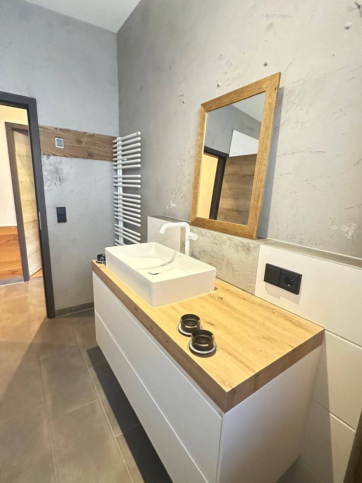 Modernes Badezimmer mit Waschtisch, Holzplatte, Spiegel und beheiztem Handtuchhalter an der Wand.
