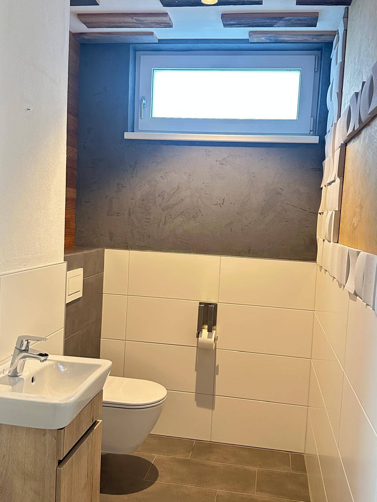 Modernes Gäste-WC mit wandhängendem WC, kleinem Waschbecken und Fenster für Tageslicht.