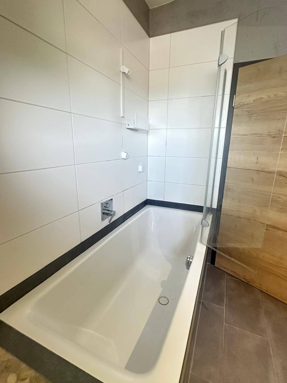 Helles Badezimmer mit Badewanne und Duschabtrennung, ausgestattet mit weißen Fliesen.