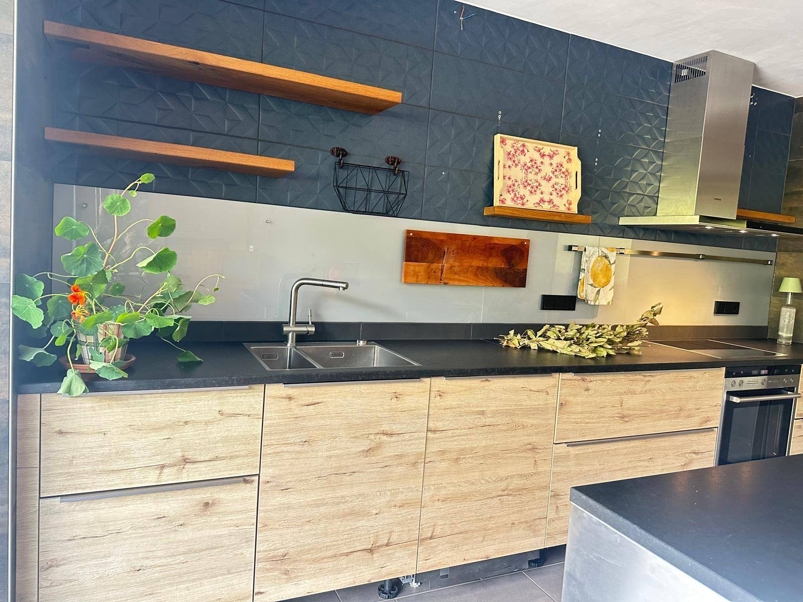 Moderne Küche mit Spülbecken, Holzregalen und dunklen Fliesen, bietet viel Arbeitsfläche.