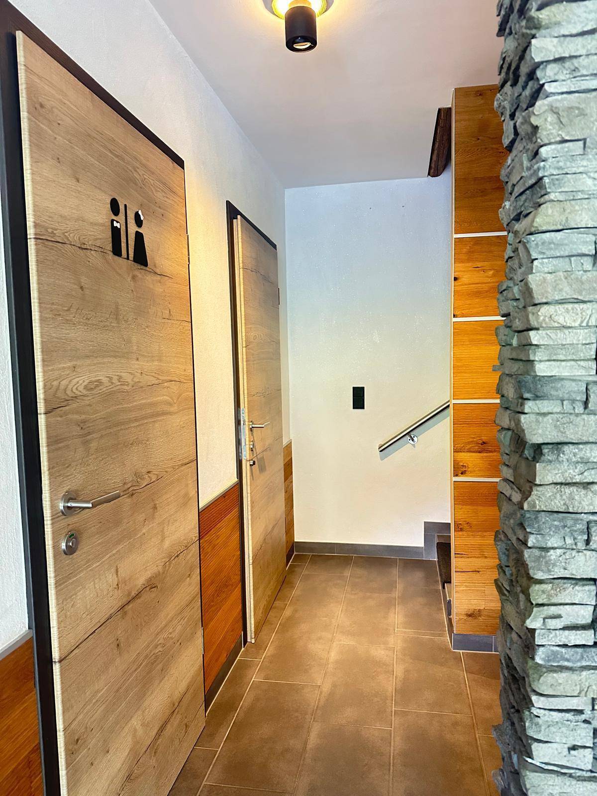 Flur mit Holztüren und Steinwand, führt zu verschiedenen Räumen im Haus.