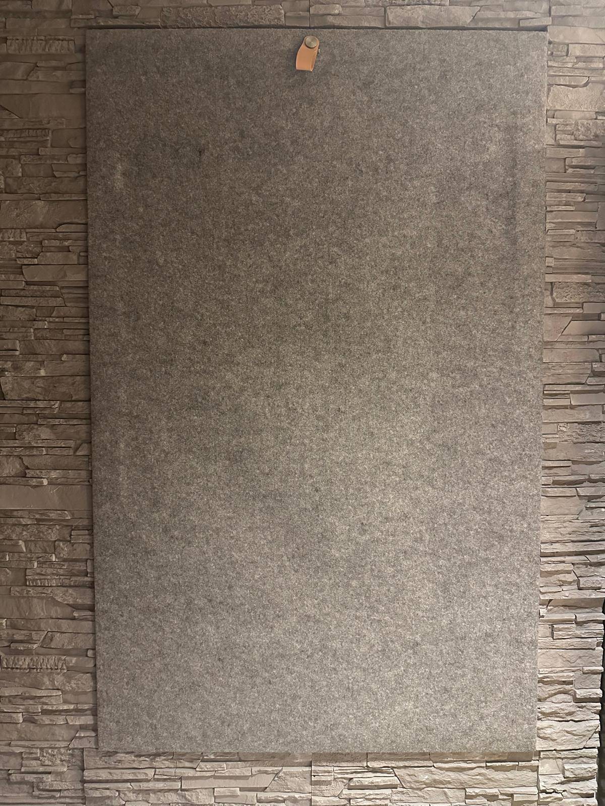 Eine graue Filzplatte an einer steinverkleideten Wand, die eine moderne Textur schafft.