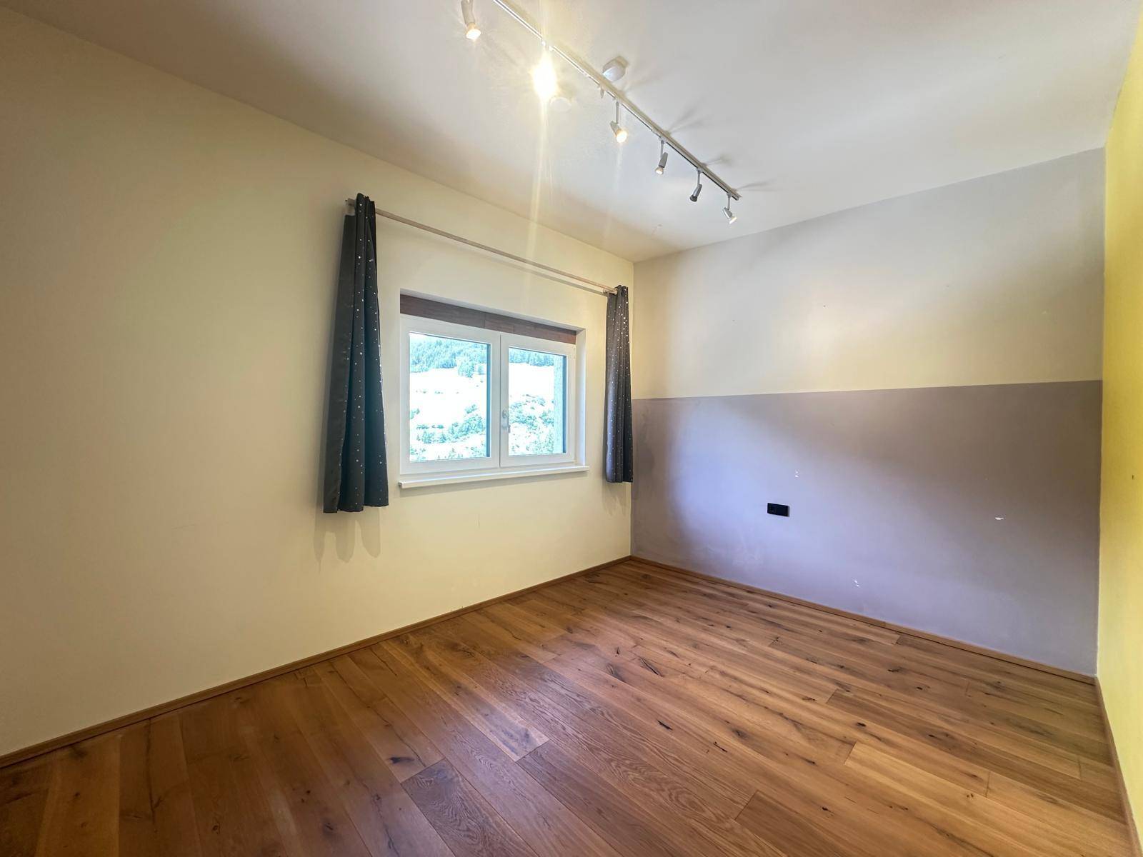Leeres Schlafzimmer mit Holzboden, Fenster und zweifarbigen Wänden, bereit zur individuellen Gestaltung.
