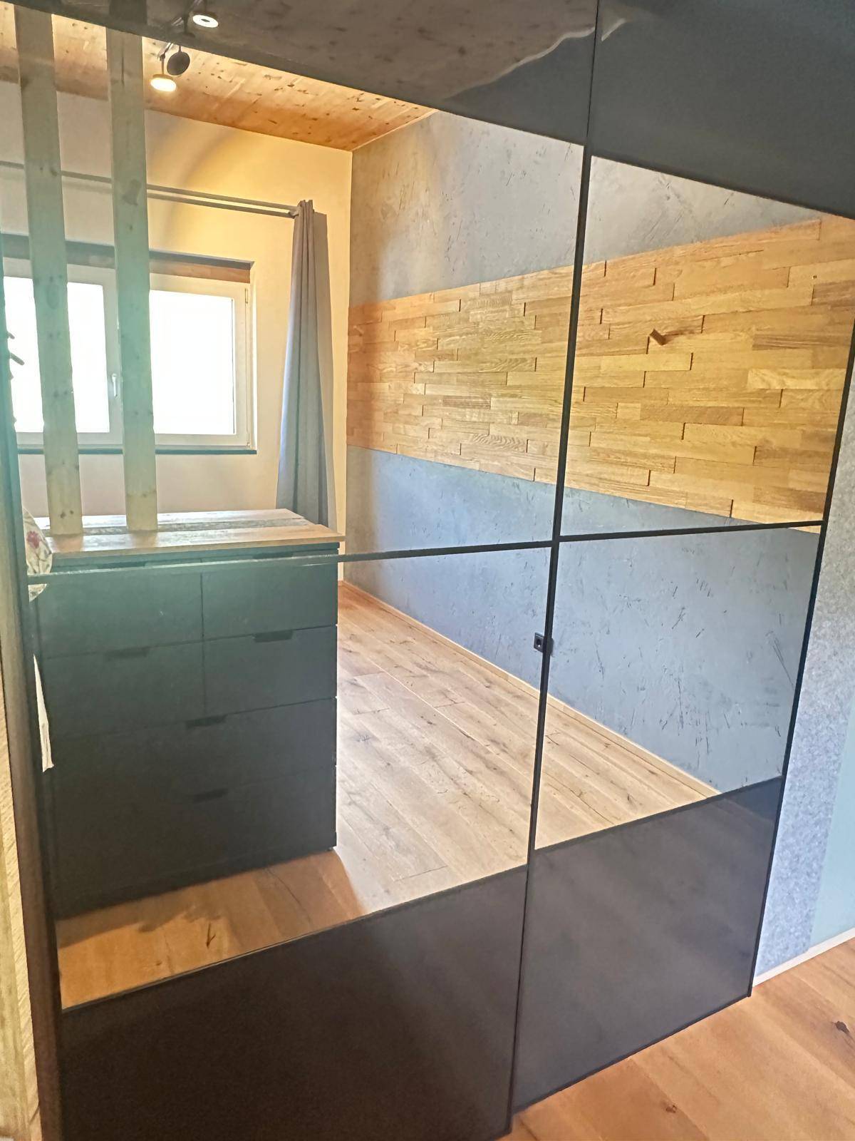 Schlafzimmer mit Holzboden, Holzdecke und einem großen Spiegelschrank, der den Raum optisch erweitert.