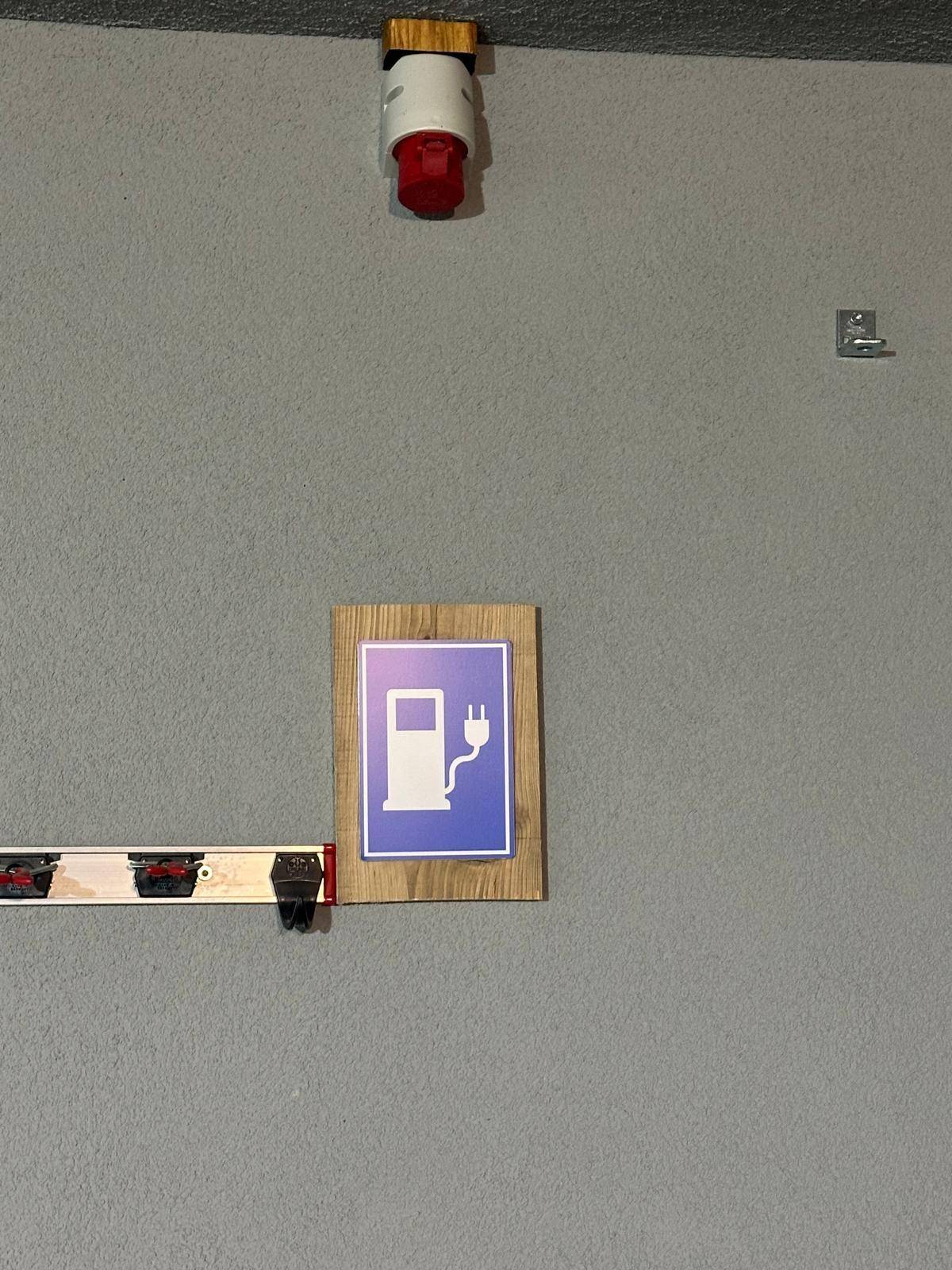 Schild für eine Ladestation für Elektrofahrzeuge an einer grauen Wand mit Industriesteckdose.