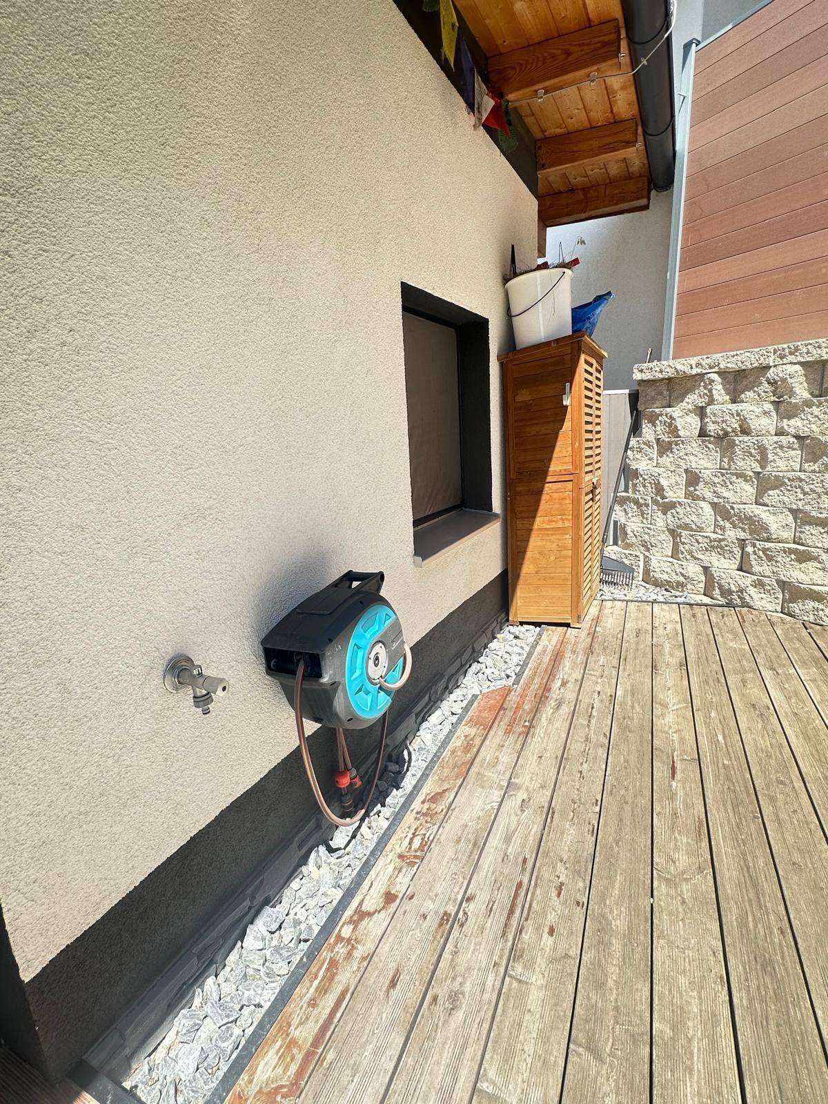 Außenbereich mit Holzterrasse, Steinwand und Gartenschlauch, praktisch und pflegeleicht.