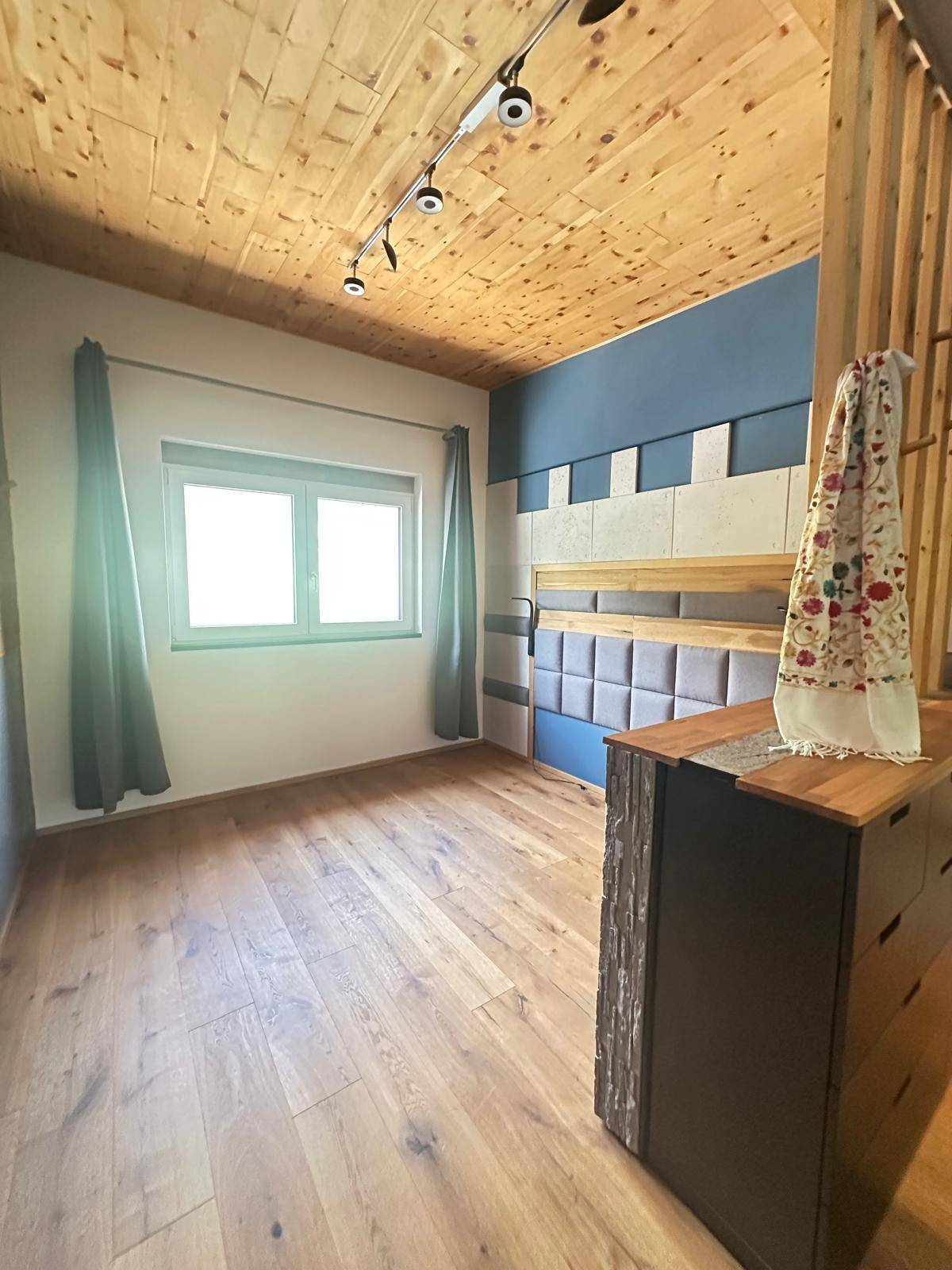Gemütliches Schlafzimmer mit Holzboden, Holzdecke und einem Fenster, das viel Tageslicht hereinlässt.