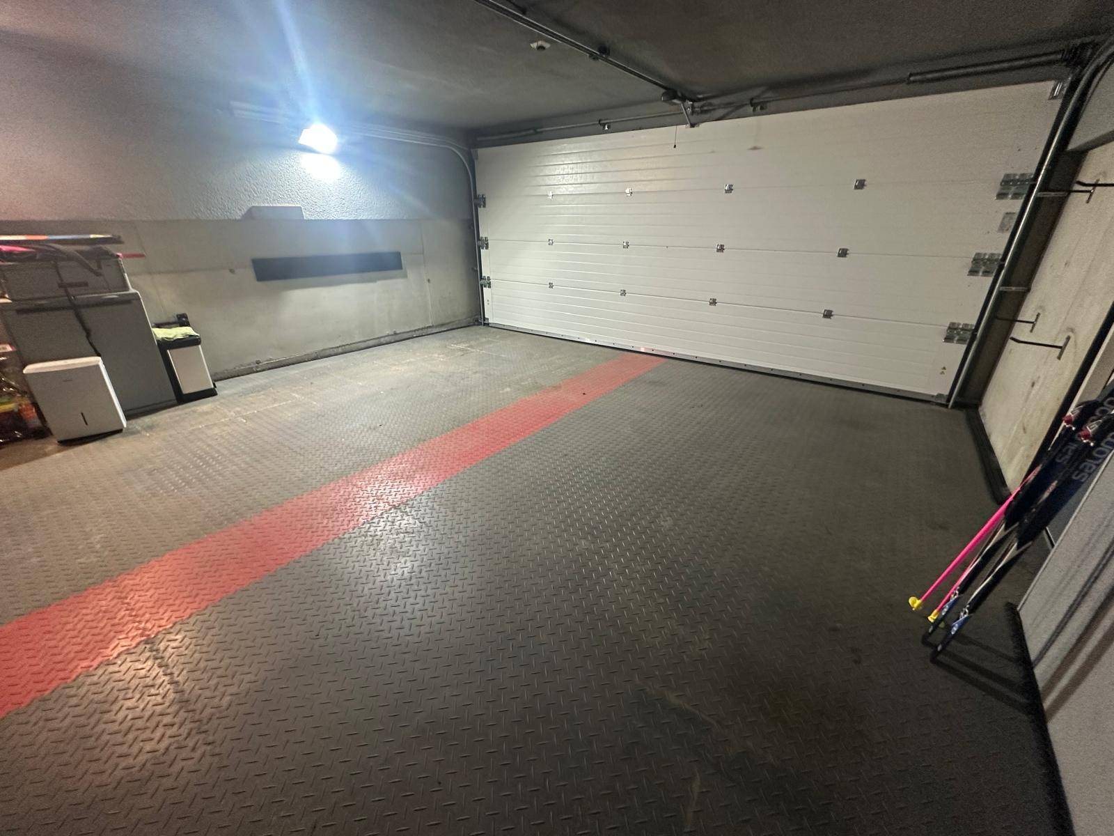 Geräumige Garage mit weißem Sektionaltor und einem robusten Boden mit roter Markierung.