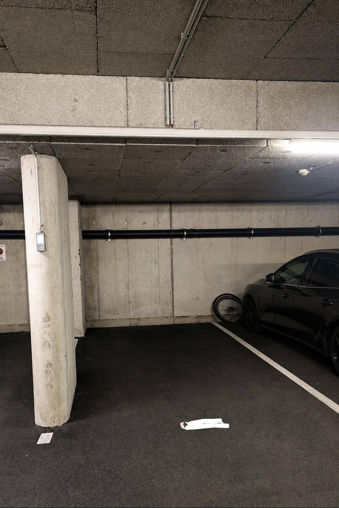 Saubere Tiefgarage mit Betonstützen und dunklem Asphaltboden, beleuchtet von Deckenleuchten.
