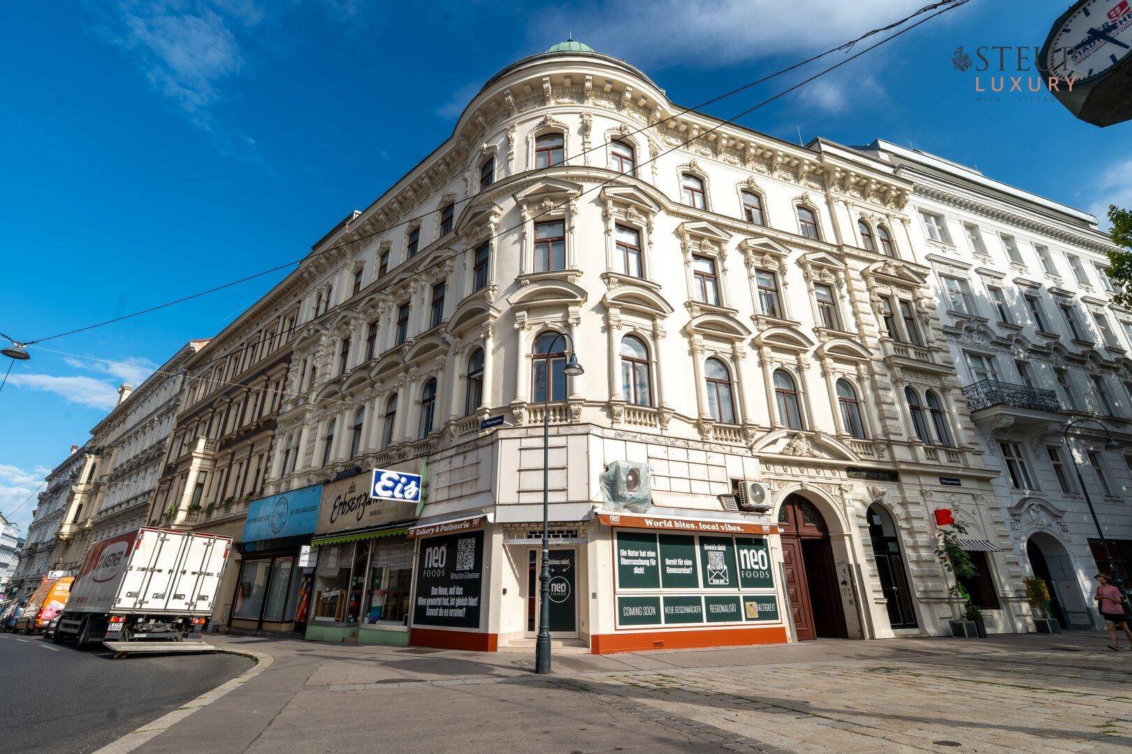 Historisches Eckgebäude mit klassischer Architektur und Geschäften im Erdgeschoss an einer belebten Straße.
