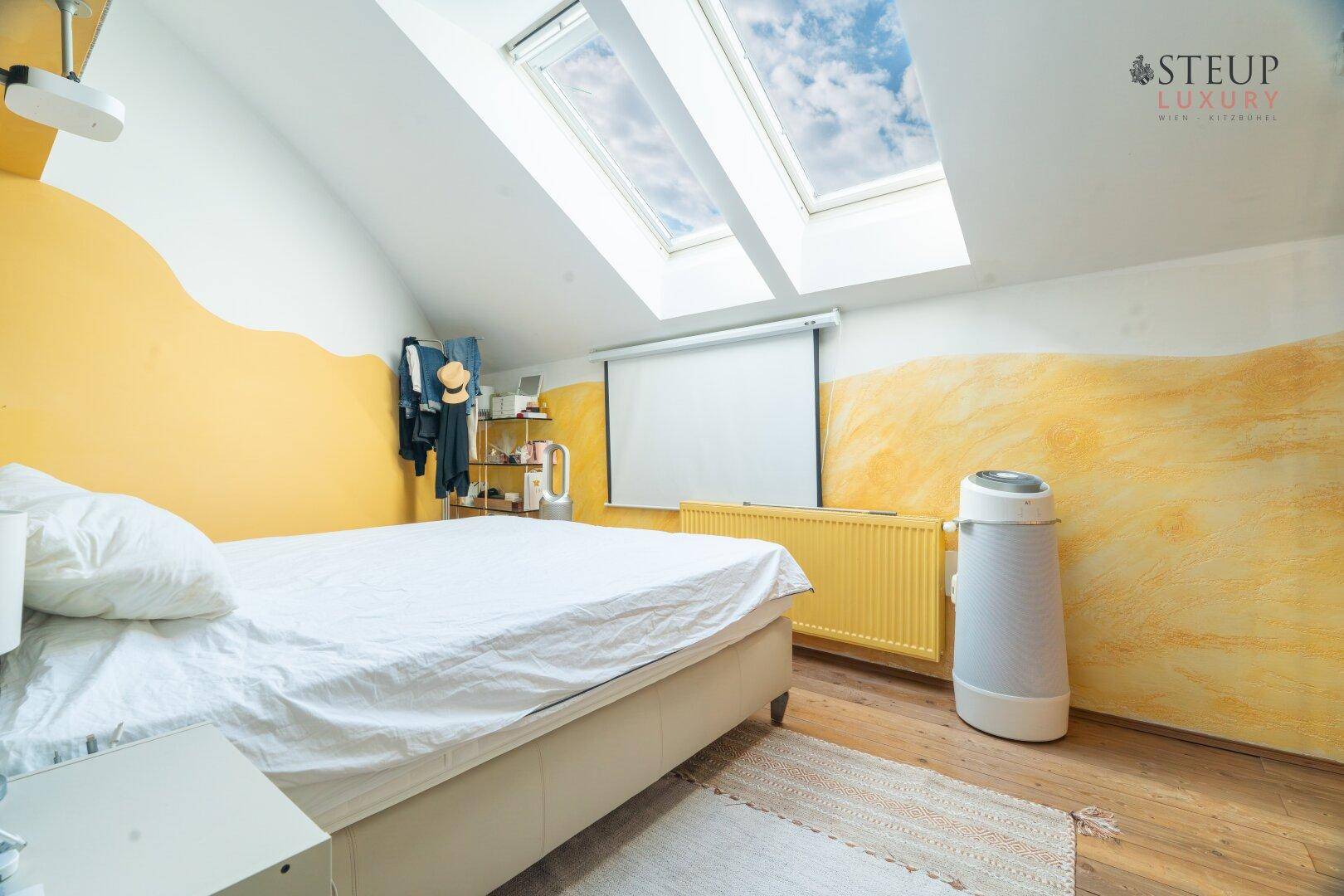Helles Schlafzimmer mit Holzboden, Dachfenstern und farbigen Wänden.
