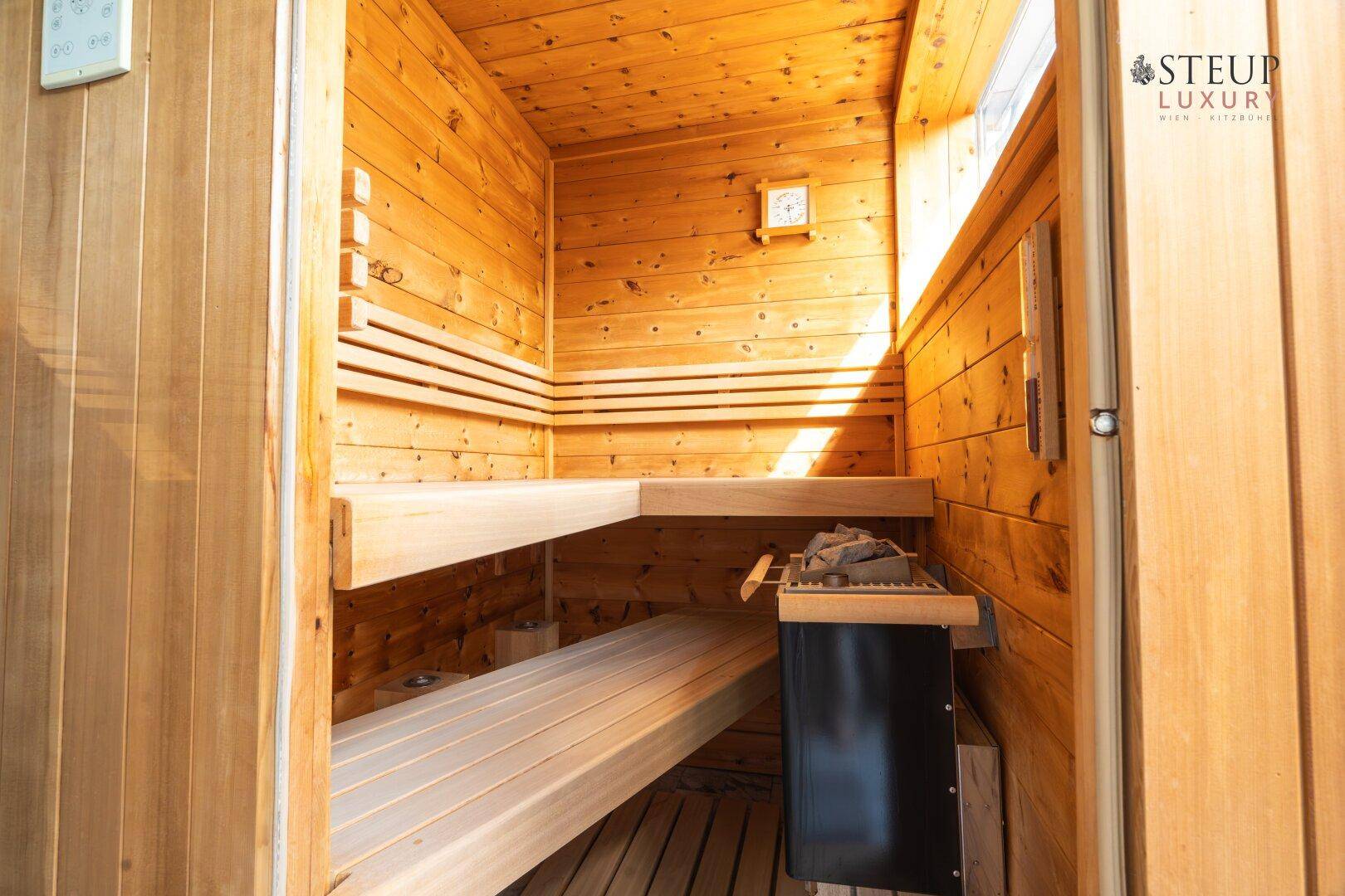 Helle Holzsauna mit mehreren Bänken und einem Saunaofen für entspannende Momente.